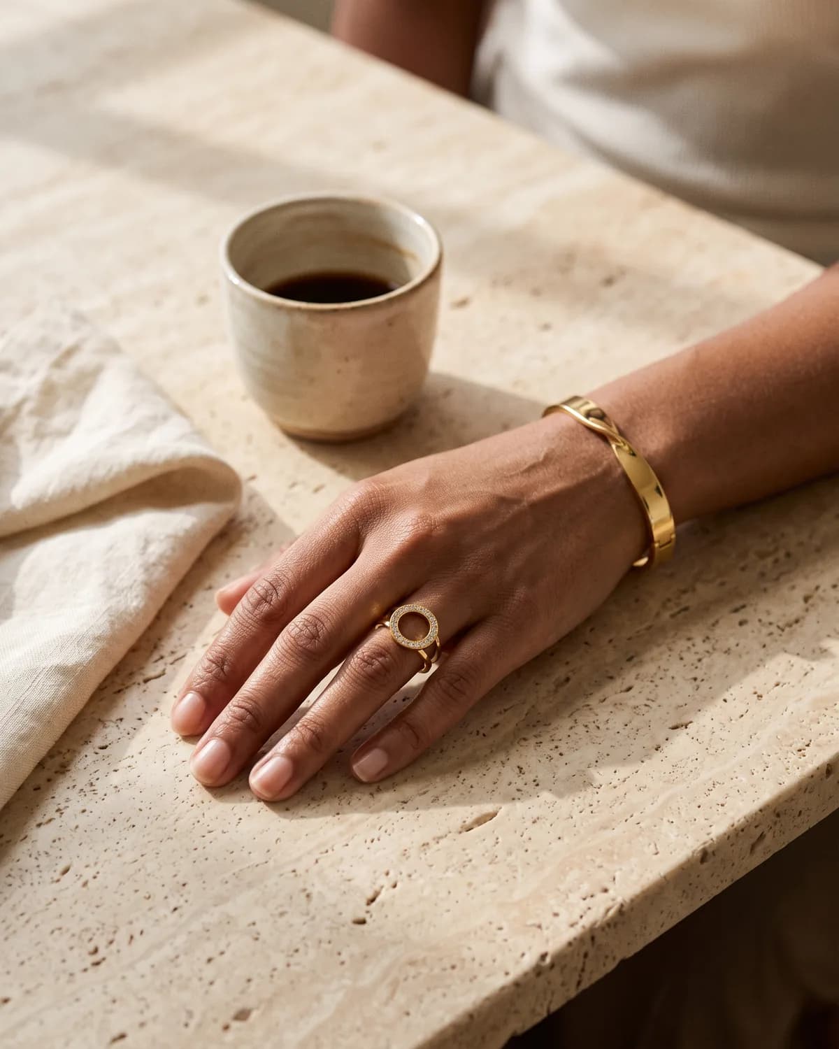 A hand wearing a CHICX ring and bangle beside a morning coffee