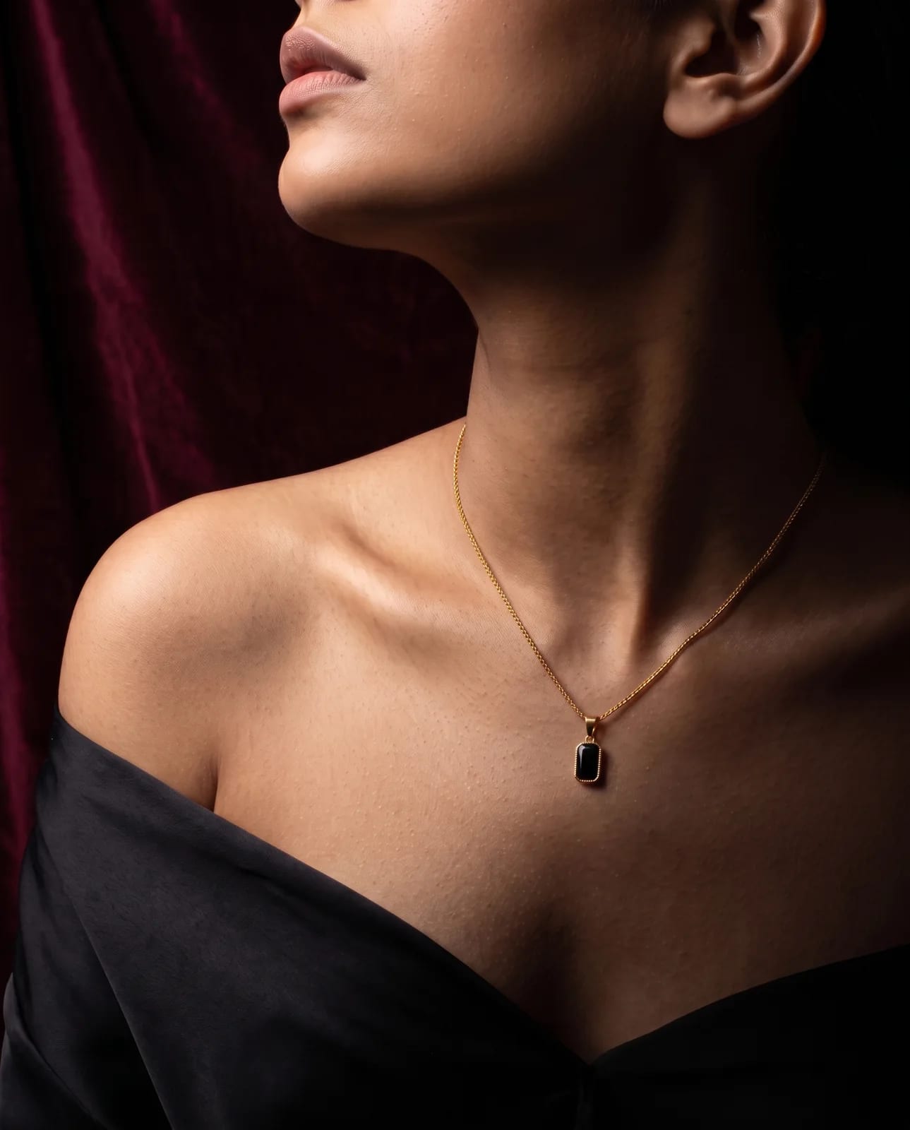Celeste Duo onyx pendant on a bare shoulder against burgundy velvet