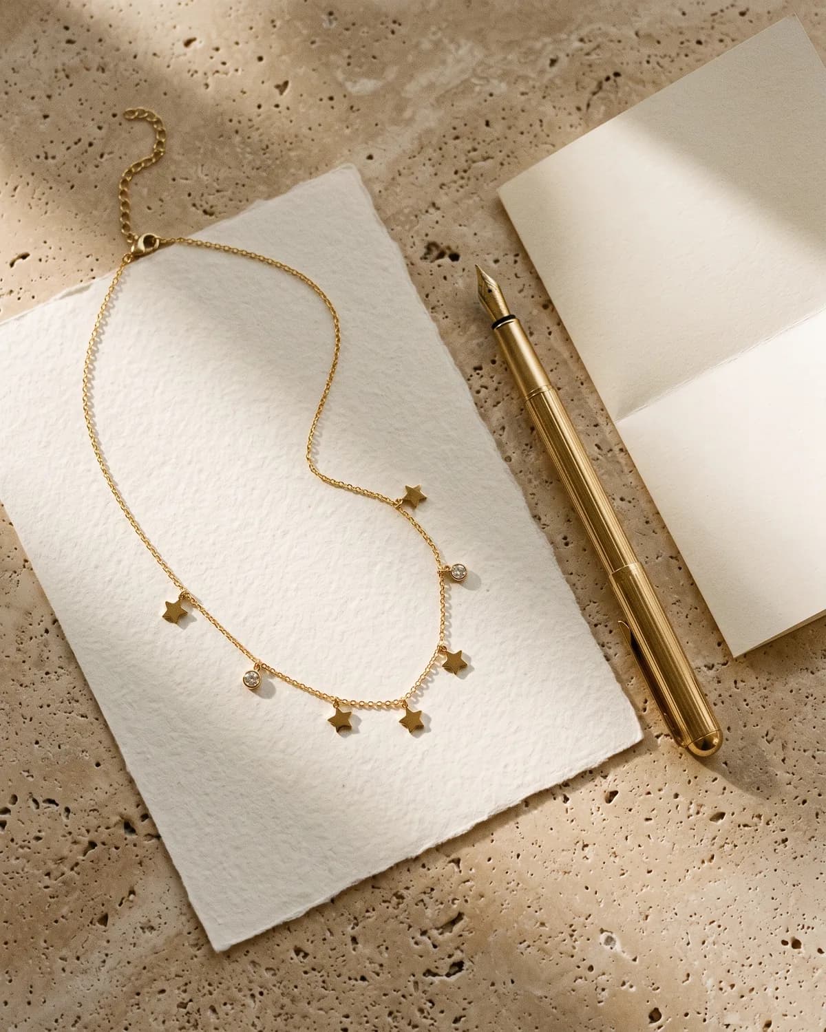 A gold star necklace on cream paper beside a fountain pen